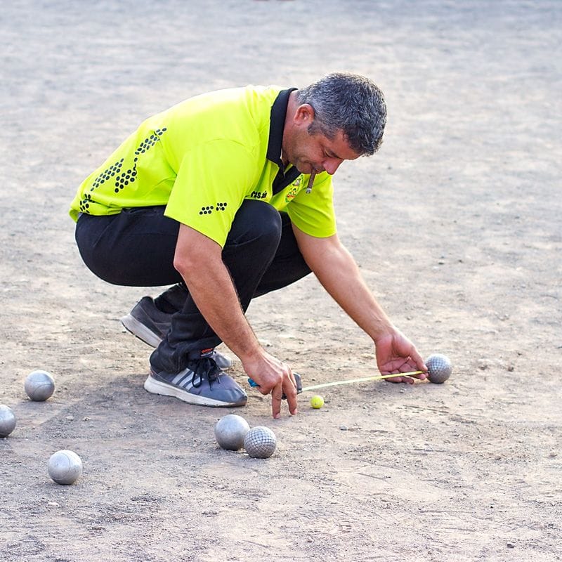 hombre midiendo la distancia entre las bolas de petanca durante un torneo